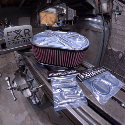 An FXR Division / TPJ Concepts Hi-FLOW PERFORMANCE AIR CLEANER for RevMax models, shown with mounting hardware, air filter, and CNC machined aluminum body, displayed on a workbench.